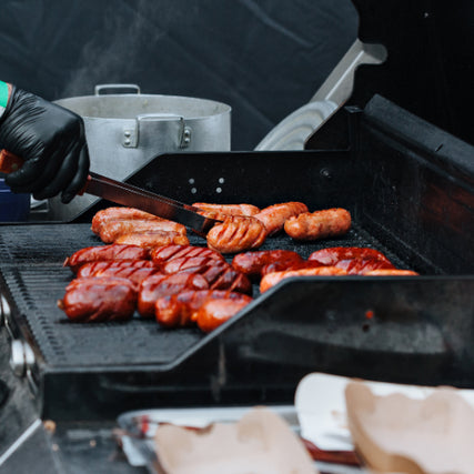 Outdoor Living SuppliesA person with a black glove grilling sausages on a barbecue grill.